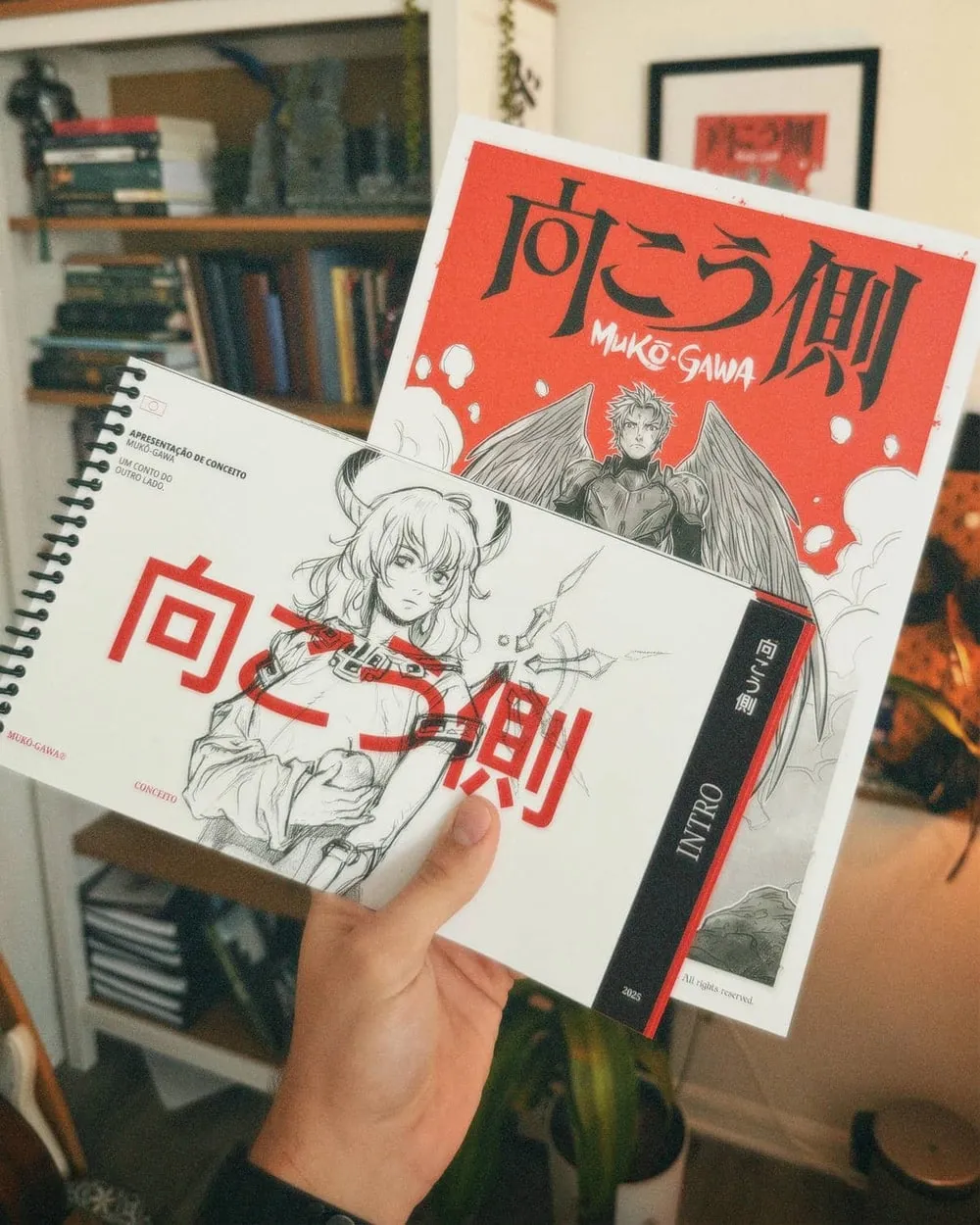 Foto do kit de Mukō-Gawa segurado na mão: a apostila conceitual em espiral, com estudo em traço na capa, sobre o print do anúncio do yomikiri, de fundo vermelho